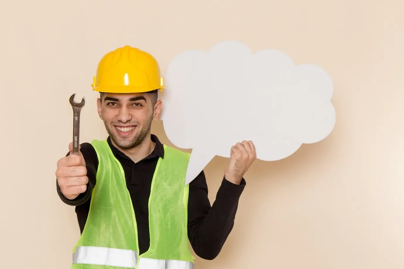 Frontansicht eines männlichen Bauarbeiters mit gelbem Helm, der ein weißes Schild und ein Werkzeug hält, vor cremefarbenem Hintergrund.